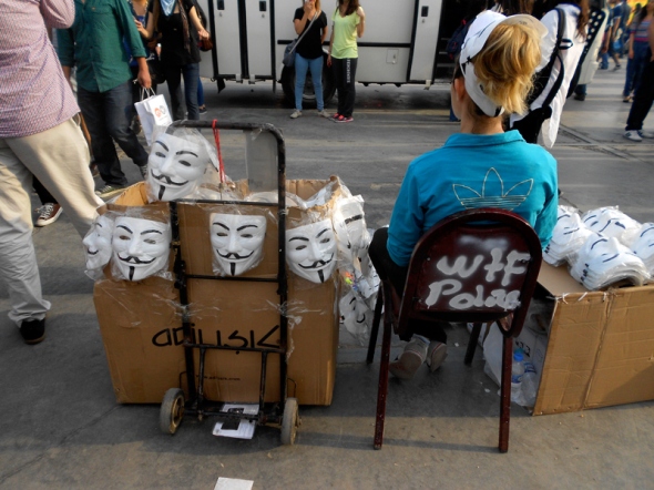 Sitting girl dirstributing Guy Fawkes masks in Taksim